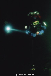 Divers working together in the intense darkness of a floo... by Michael Grebler 